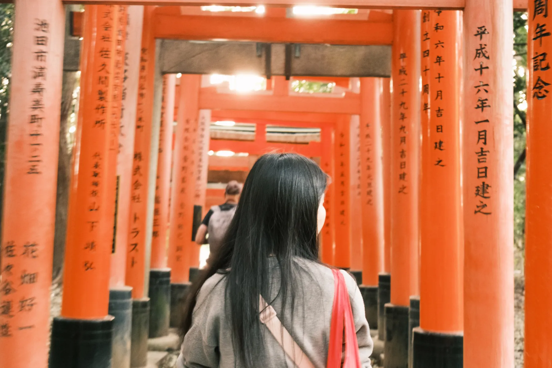 A visitor walking beneath a dense passage of vermilion torii gates.